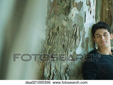 Man leaning against tree trunk, eyes closed View Large Photo Image Stock Photograph - Man leaning against tree trunk, eyes closed. Fotosearch
