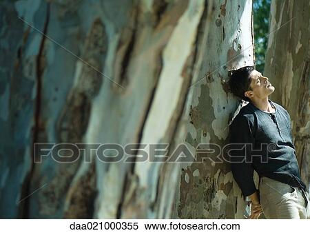 Stock Photography - Man leaning against tree trunk, eyes closed. Fotosearch