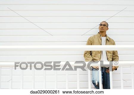 Stock Image - Man leaning against wall, hands on hips, looking away. Fotosearch