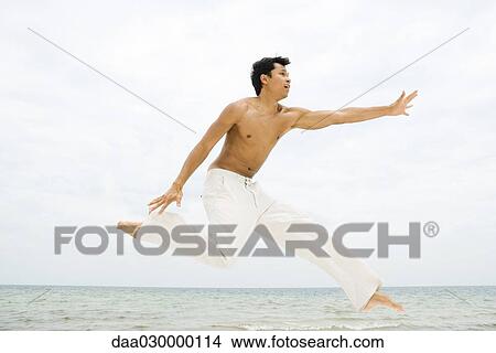 Man leaping in the air, side view, ocean in background View Large Photo Image Picture - Man leaping in the air, side view, ocean in background. Fotosearch