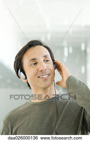 Man listening to headphones, looking away, smiling View Large Photo Image Stock Photograph - Man listening to headphones, looking away, smiling. Fotosearch