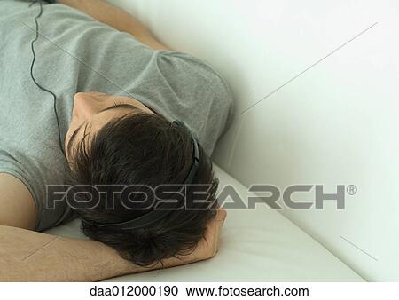 Man lying down, listening to headphones View Large Photo Image Stock Image - Man lying down, listening to headphones. Fotosearch