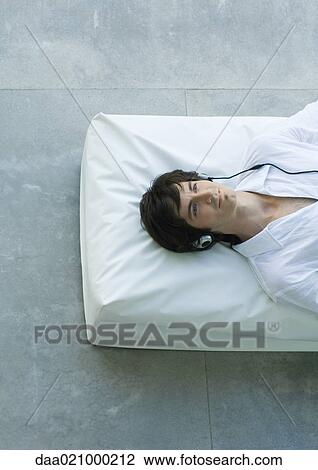 Stock Image - Man lying down listening to headphones. Fotosearch