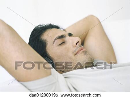 Man lying down, listening to headphones with hands behind head View Large Photo Image Stock Photography - Man lying down, listening to headphones with hands behind head. Fotosearch
