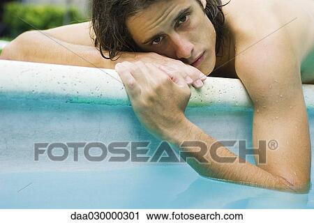 Man lying on edge of pool with elbow dangling in water, looking at camera View Large Photo Image Stock Image - Man lying on edge of pool with elbow dangling in water, looking at camera. Fotosearch