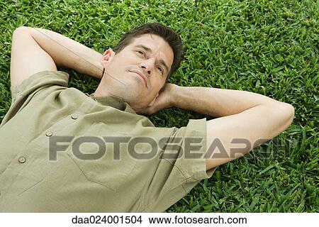 Man lying on grass, hands behind head View Large Photo Image Picture - Man lying on grass, hands behind head. Fotosearch