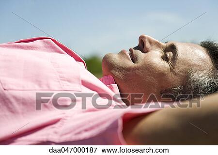 Man lying outdoors in sun with hands behind head View Large Photo Image Stock Photo - Man lying outdoors in sun with hands behind head. Fotosearch