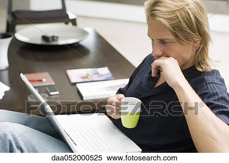 Stock Photography - Man on sofa with laptop computer and cup of coffee. Fotosearch