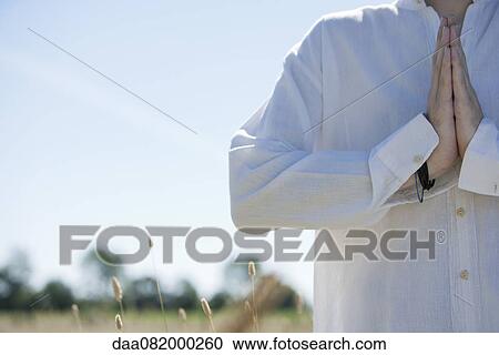 Stock Image - Man outdoors with hands clasped in prayer, cropped. Fotosearch