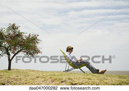 Man relaxing in lounge chair outdoors writing in notebook View Large Photo Image Stock Image - Man relaxing in lounge chair outdoors writing in notebook. Fotosearch