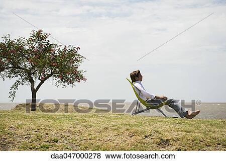 Man relaxing in lounge chair outdoors contemplating sea shore view View Large Photo Image Stock Photo - Man relaxing in lounge chair outdoors contemplating sea shore view. Fotosearch