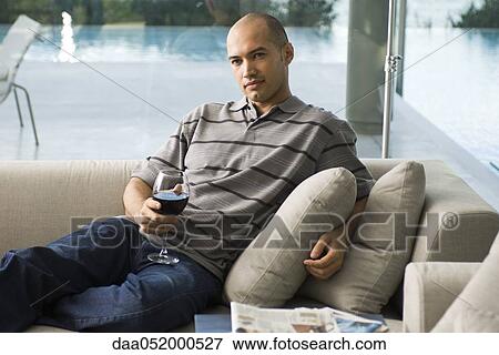Man relaxing on sofa with glass of wine View Large Photo Image Stock Photo - Man relaxing on sofa with glass of wine. Fotosearch