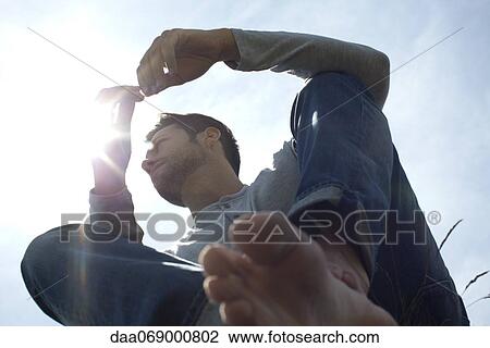 Man relaxing outdoors, backlit by sun, low angle view View Large Photo Image Stock Image - Man relaxing outdoors, backlit by sun, low angle view. Fotosearch