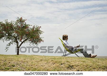 Man relaxing outdoors looking at cell phone View Large Photo Image Stock Image - Man relaxing outdoors looking at cell phone. Fotosearch
