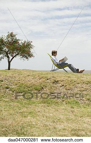 Man relaxing outdoors reading through binder View Large Photo Image Stock Image - Man relaxing outdoors reading through binder. Fotosearch