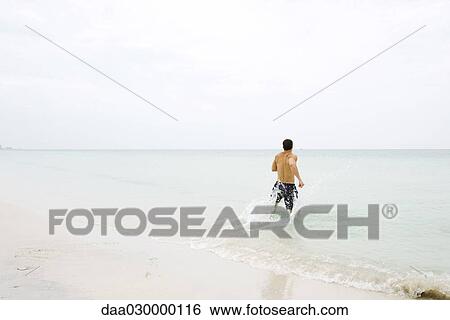Man running in shallow water at the beach, rear view View Large Photo Image Stock Photograph - Man running in shallow water at the beach, rear view. Fotosearch