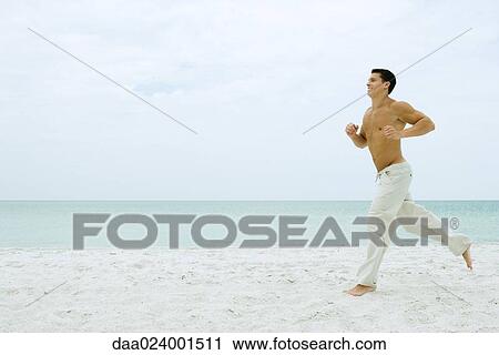 Stock Image - Man running on beach, full length, side view. Fotosearch
