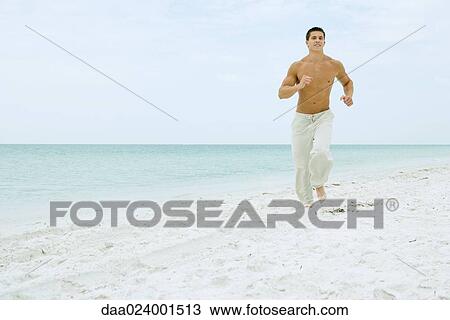Man running on beach, smiling at camera, full length View Large Photo Image Stock Image - Man running on beach, smiling at camera, full length. Fotosearch