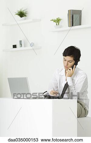 Man sitting at desk talking on landline phone, looking down at agenda View Large Photo Image Stock Image - Man sitting at desk talking on landline phone, looking down at agenda. Fotosearch