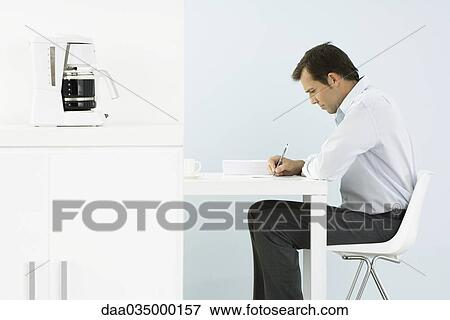 Man sitting at desk writing, side view View Large Photo Image Stock Photo - Man sitting at desk writing, side view. Fotosearch