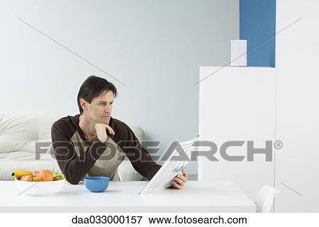 Man sitting at table, reading newspaper View Large Photo Image Stock Photo - Man sitting at table, reading newspaper. Fotosearch