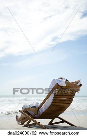 Stock Image - Man sitting in deck chair, facing sea. Fotosearch
