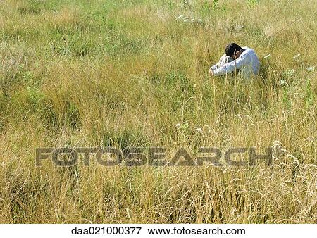 Man sitting in field, hugging knees with head down View Large Photo Image Stock Photo - Man sitting in field, hugging knees with head down. Fotosearch
