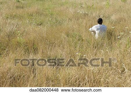 Stock Photo - Man sitting in field, rear view. Fotosearch