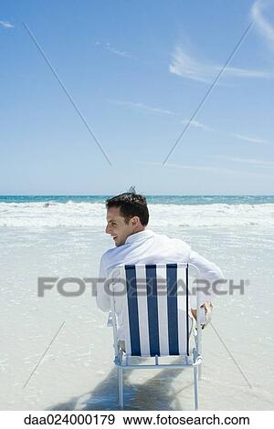 Man sitting in folding chair on beach, rear view View Large Photo Image Stock Photo - Man sitting in folding chair on beach, rear view. Fotosearch