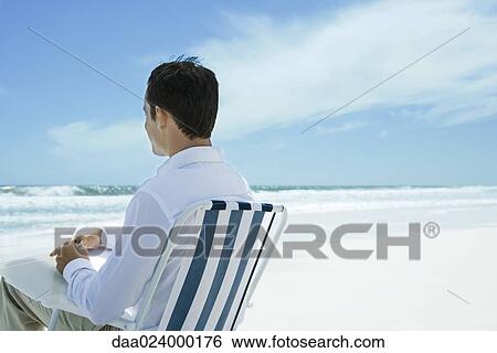 Man sitting in folding chair on beach, using pen and paper, rear view View Large Photo Image Stock Photograph - Man sitting in folding chair on beach, using pen and paper, rear view. Fotosearch