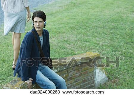 Man sitting in park, listening to headphones while woman walks by View Large Photo Image Stock Image - Man sitting in park, listening to headphones while woman walks by. Fotosearch