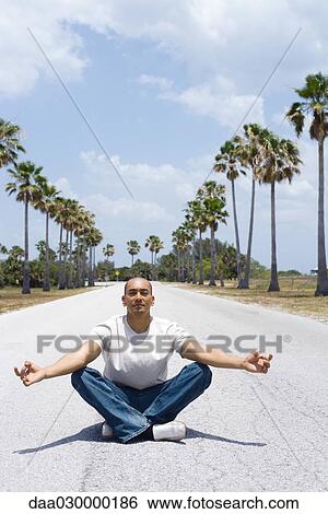 Stock Photograph - Man sitting in the middle of the road in lotus position. Fotosearch