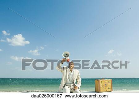 Man sitting next to suitcase at the beach, shouting into megaphone View Large Photo Image Stock Photo - Man sitting next to suitcase at the beach, shouting into megaphone. Fotosearch