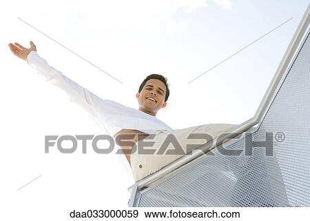 Man sitting on balcony, one arm raised, low angle view View Large Photo Image Stock Photo - Man sitting on balcony, one arm raised, low angle view. Fotosearch