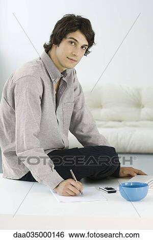 Man sitting on coffee table, writing, looking at camera View Large Photo Image Stock Photograph - Man sitting on coffee table, writing, looking at camera. Fotosearch