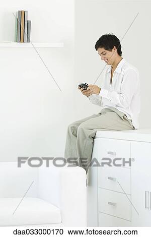 Man sitting on counter, playing handheld video game View Large Photo Image Stock Image - Man sitting on counter, playing handheld video game. Fotosearch