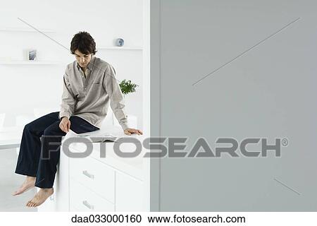 Man sitting on counter, reading newspaper View Large Photo Image Stock Image - Man sitting on counter, reading newspaper. Fotosearch