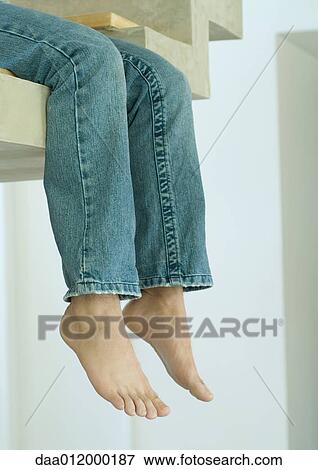 Stock Photo - Man sitting on edge of staircase, legs dangling, low section. Fotosearch
