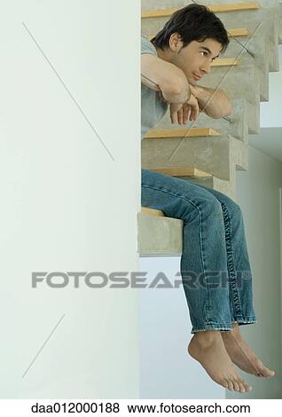 Stock Photo - Man sitting on edge of staircase, legs dangling. Fotosearch