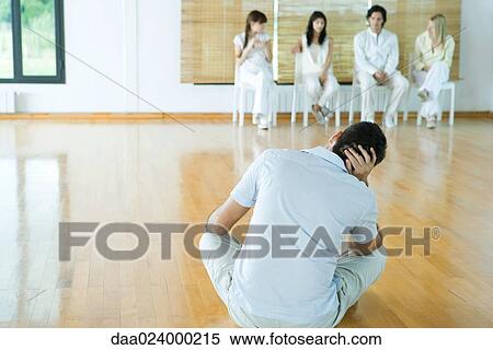Stock Photography - Man sitting on floor, facing group sitting in chairs. Fotosearch