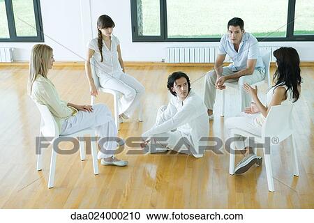 Man sitting on floor in middle of group sitting in chairs, talking View Large Photo Image Stock Image - Man sitting on floor in middle of group sitting in chairs, talking. Fotosearch