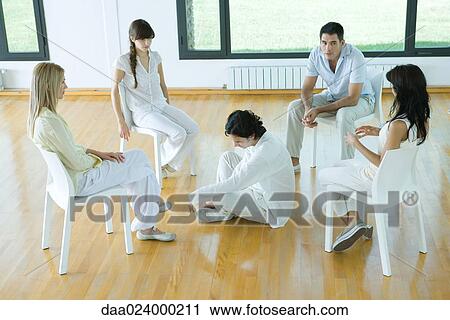 Man sitting on floor in middle of group sitting in chairs, talking View Large Photo Image Stock Image - Man sitting on floor in middle of group sitting in chairs, talking. Fotosearch