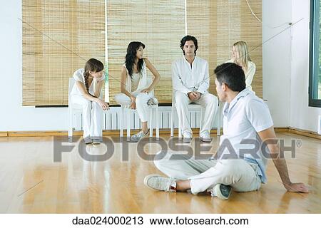 Man sitting on floor, looking over shoulder at group sitting in chairs View Large Photo Image Stock Image - Man sitting on floor, looking over shoulder at group sitting in chairs. Fotosearch