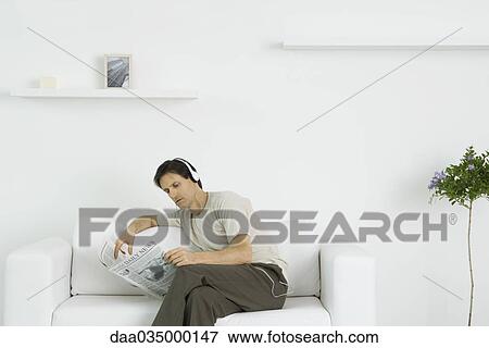 Man sitting on loveseat, reading newspaper, listening to headphones View Large Photo Image Stock Photo - Man sitting on loveseat, reading newspaper, listening to headphones. Fotosearch