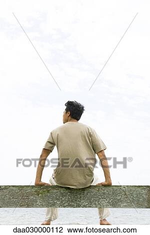 Man sitting on rail, facing ocean, rear view View Large Photo Image Stock Image - Man sitting on rail, facing ocean, rear view. Fotosearch