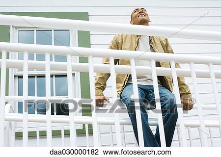 Man sitting on railing, smiling, looking up View Large Photo Image Stock Image - Man sitting on railing, smiling, looking up. Fotosearch