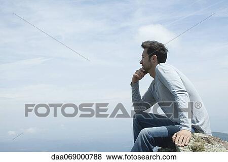 Stock Photo - Man sitting on rock, contemplating view. Fotosearch