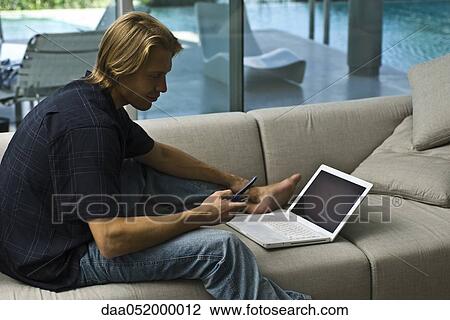 Man sitting on sofa with laptop nearby, using cell phone View Large Photo Image Stock Image - Man sitting on sofa with laptop nearby, using cell phone. Fotosearch