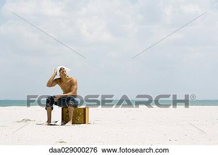 Man sitting on suitcase at the beach, covering head with handkerchief, looking up at sun View Large Photo Image Stock Photograph - Man sitting on suitcase at the beach, covering head with handkerchief, looking up at sun. Fotosearch