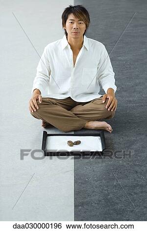 Man sitting on the ground in front of rock garden, looking at camera View Large Photo Image Stock Photograph - Man sitting on the ground in front of rock garden, looking at camera. Fotosearch
